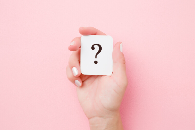 Card of question mark in young woman hand on pastel pink background