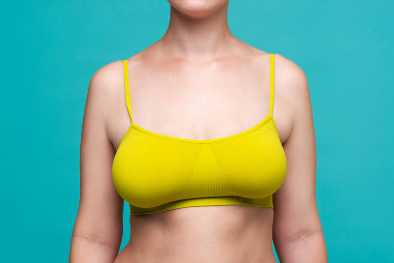 Woman in yellow top bra with big natural breasts on blue background