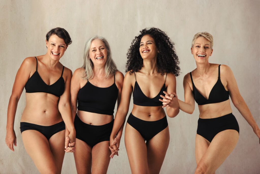women smiling cheerfully while wearing black underwear and holding hands together in a studio